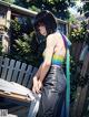 A woman in a rainbow top and jeans standing next to a fence.