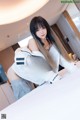A woman in a white jacket is posing on a bed.