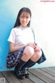 A young woman in a school uniform sitting on a wooden floor.