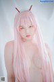 A woman with long pink hair wearing a devil horns headband.