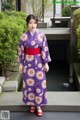 A woman in a purple kimono standing in front of a pond.