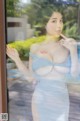 A woman in a blue dress standing by a window.