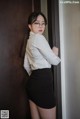 A woman in a white shirt and black skirt leaning against a wall.