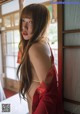 A woman in a red kimono standing in front of a window.